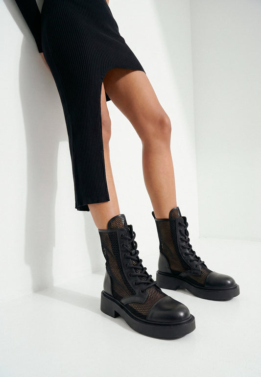 Black leather mesh combat boots worn with a black dress, close styling view