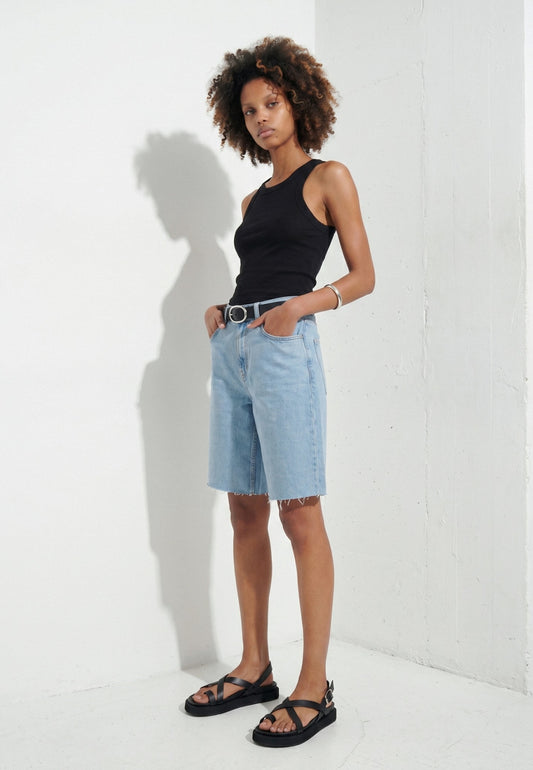 Woman wearing black toe-loop leather flatform sandals with denim shorts in a white studio