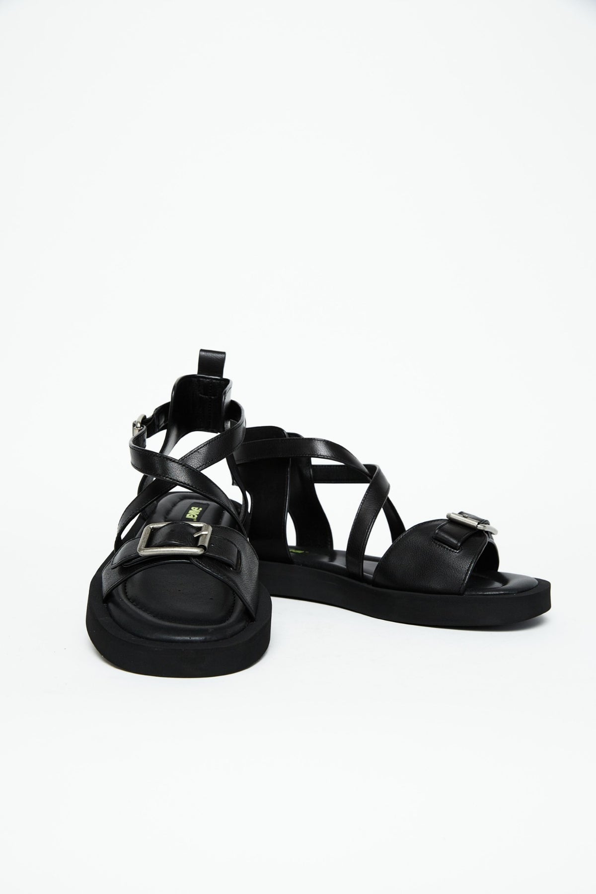 Front view of black leather sandals showing wide buckle straps and crossover construction