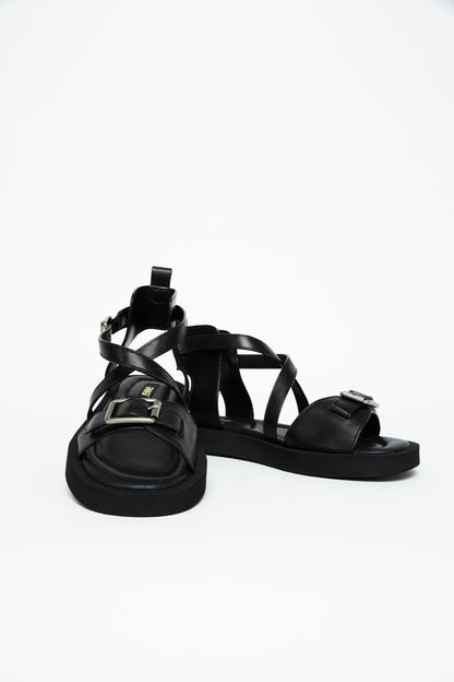 Front view of black leather sandals showing wide buckle straps and crossover construction
