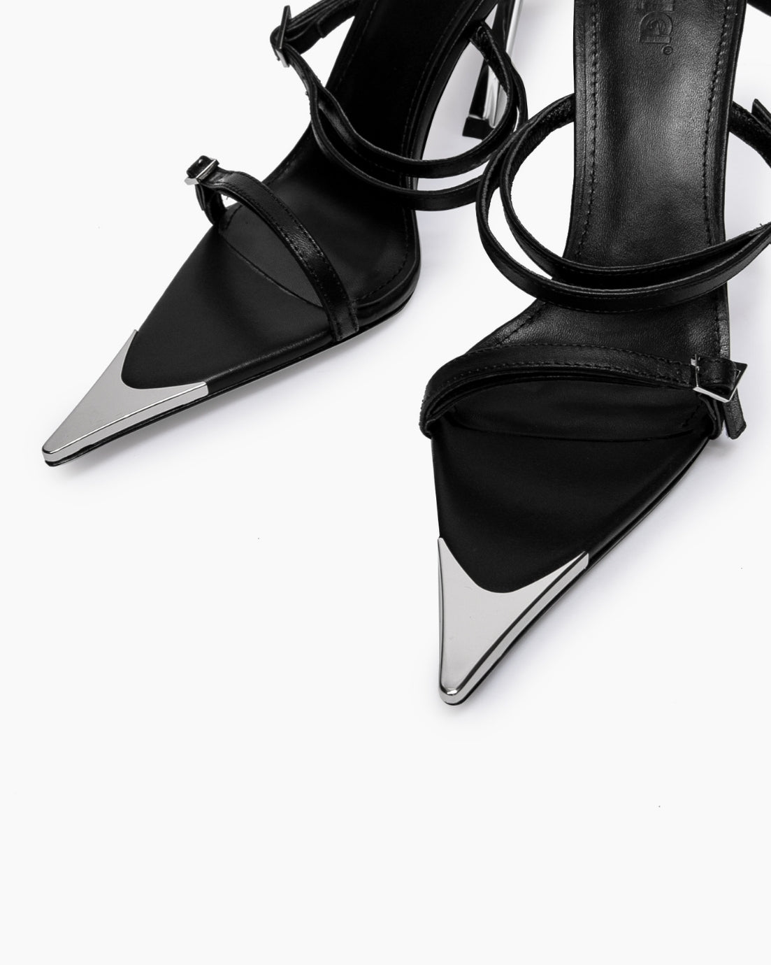 Close-up of black leather straps, small buckles and mirrored pointed toe caps