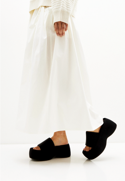 Black textile platform slides styled on a model with an ivory skirt, side view