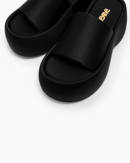 Close-up of black platform slides showing the broad textile strap and footbed