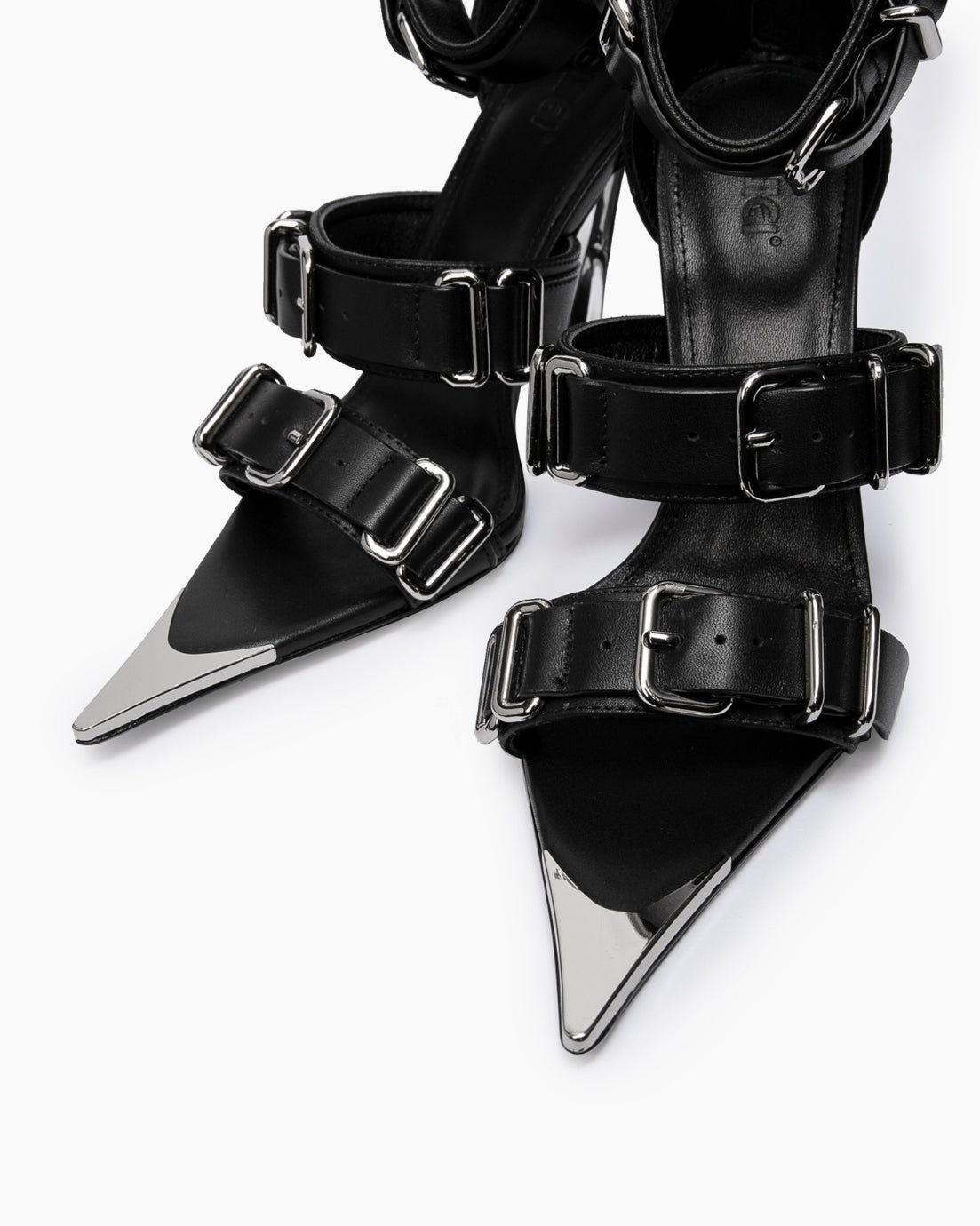Close-up of wide black leather straps, oversized chrome buckles and pointed toe caps