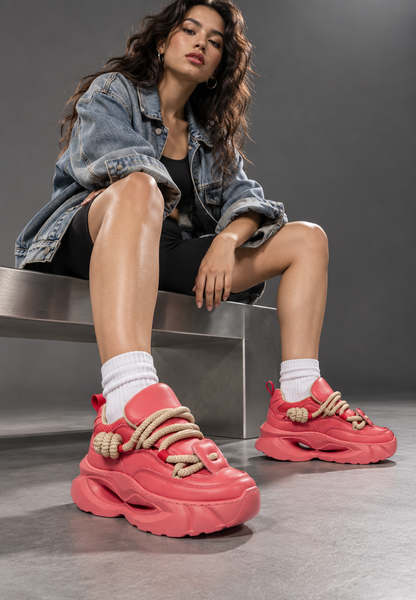 Seated model wearing coral rope-lace sneakers in an industrial studio