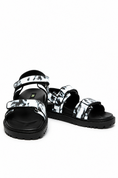 Front angle of black and white brush-print leather sandals with adjustable tabs