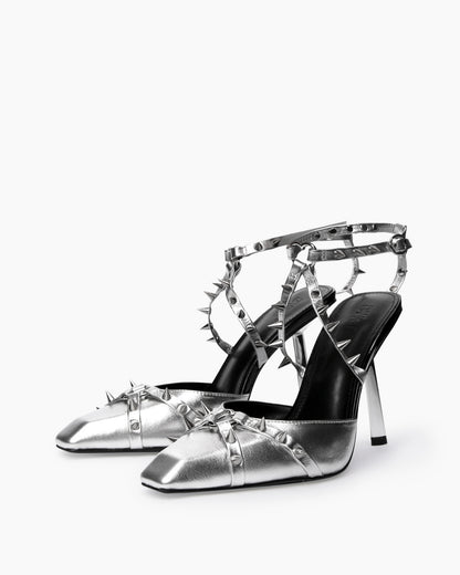 Pair of silver leather heels with heart-shaped rings and crossed spiked straps, three-quarter view