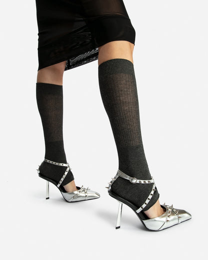 Silver spiked heels on a standing model, showing the buckled ankle straps and open backs