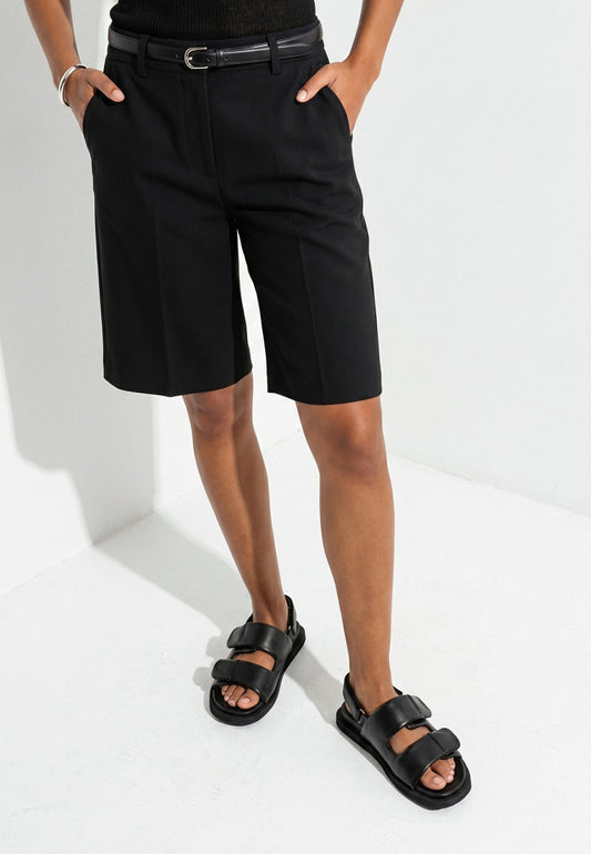 Woman wearing black padded leather sandals with tailored shorts in a white studio